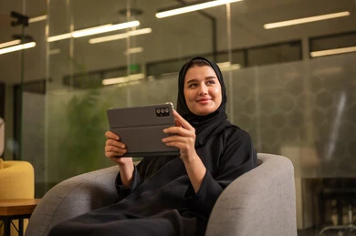 Integrating modern technologies in the administrative and office field, Gulf companies and offices in Saudi Arabia, a remote work session, an Arab Saudi Gulf woman in a hijab wearing a black abaya using a tablet device.