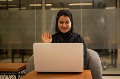 امراة عربية خليجية سعودية محجبة تجلس في المكتب تقوم بالعمل عبر اللابتوب، دمج العمل مع التقنية والتكنولوجيا، توفير بيئة عمل مريحة ومناسبة، استخدام جهاز الحاسوب المحمول لإنجاز المهام باحترافية، التوظيف في المكاتب والشركات السعودية