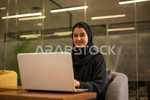 توفير بيئة عمل مريحة ومناسبة، دمج العمل مع التقنية والتكنولوجيا، استخدام جهاز الحاسوب المحمول لإنجاز المهام باحترافية، امراة عربية خليجية سعودية محجبة تجلس في المكتب تقوم بالعمل عبر اللابتوب، التوظيف في المكاتب والشركات السعودية