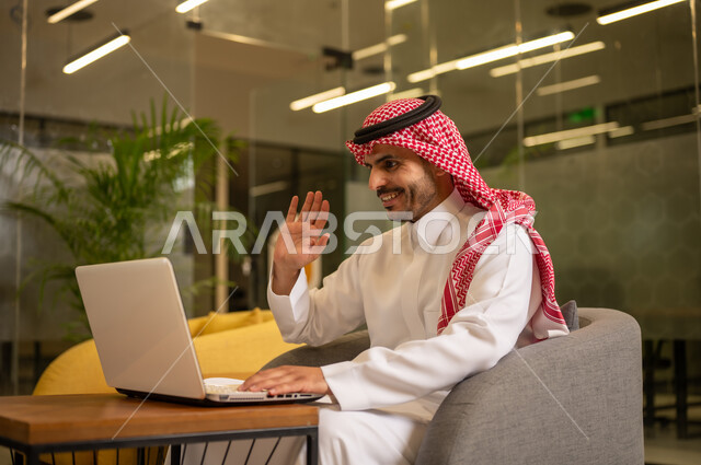 Using a laptop to accomplish tasks professionally, office jobs and work, providing a comfortable and suitable work environment, an Arab Gulf Saudi man wearing traditional thobe and ghutrah sitting at the office working on the laptop, employment in Saudi offices and companies.
