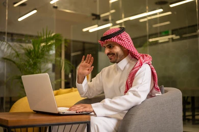 استخدام جهاز الحاسوب المحمول لإنجاز المهام باحترافية، مهن وأعمال مكتبية، توفير بيئة عمل مريحة ومناسبة،رجل عربي خليجي سعودي يرتدي الثوب والشماغ التقليدي يجلس في المكتب يقوم بالعمل عبر اللابتوب، التوظيف في المكاتب والشركات السعودية
