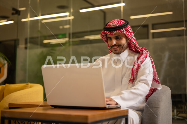 مهن وأعمال مكتبية، توفير بيئة عمل مريحة ومناسبة، استخدام جهاز الحاسوب المحمول لإنجاز المهام باحترافية، رجل عربي خليجي سعودي يرتدي الثوب والشماغ التقليدي يجلس في المكتب يقوم بالعمل عبر اللابتوب، التوظيف في المكاتب والشركات السعودية