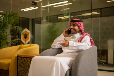العمل في المجال المكتبي, إيماءات الجودة والرضا والقبول, رجل عربي خليجي سعودي مبتسم يرتدي الثوب التقليدي والشماغ يقوم بإجراء مكالمة هاتفية عبر الهاتف المحمول,متابعه الأعمال الادارية