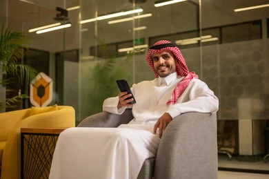 رجل عربي خليجي سعودي مبتسم يرتدي الثوب التقليدي والشماغ يقوم بإجراء مكالمة هاتفية عبر الهاتف المحمول, العمل في المجال المكتبي, متابعه الأعمال الادارية