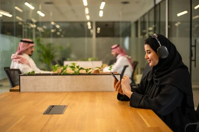 مهن ووظائف نسائية, متابعة وتطوير الأعمال، الإجابة على استفسارات العملاء, موظفة عربية خليجية سعودية مبتسمة ترتدي العباءة والحجاب تضع سماعات الرأس (الهيدفون) تستخدم الهاتف المحمول، العمل في المجال المكتبي