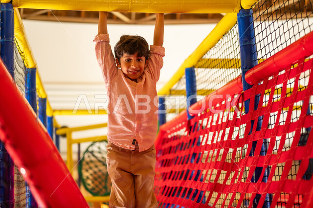 Saudi Boy Hanging from Bars at Indoor Playground