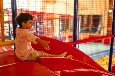 طفل عربي على زلاقة حمراء في منطقة ألعاب داخلية