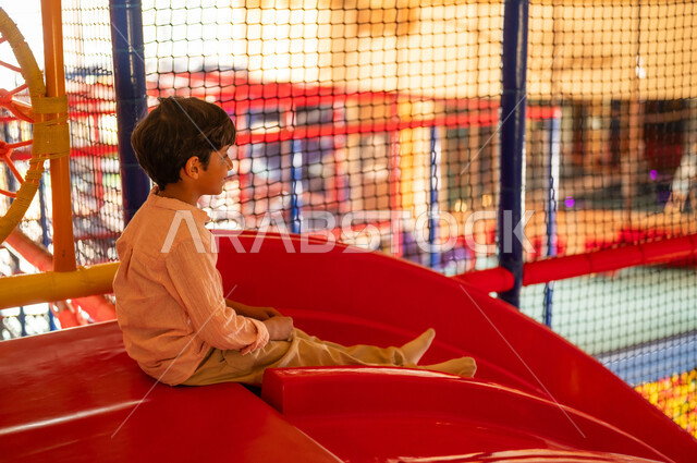 Saudi Boy Sitting on Red Slide in Indoor Playground