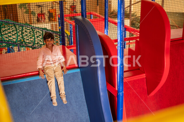 Saudi Boy Sitting on Slide in Indoor Playground