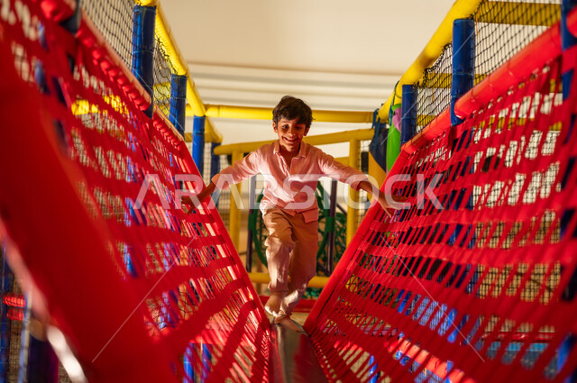 Arab Boy Playing on Netted Bridge in Indoor Playground