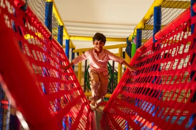 طفل عربي يلعب على جسر شبكي في منطقة ألعاب داخلية