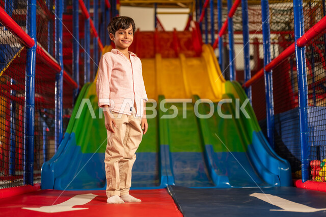 طفل عربي في منطقة ألعاب داخلية بجانب منزلقة ملونة