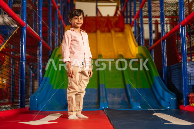 Saudi Boy Standing at Indoor Playground Slide