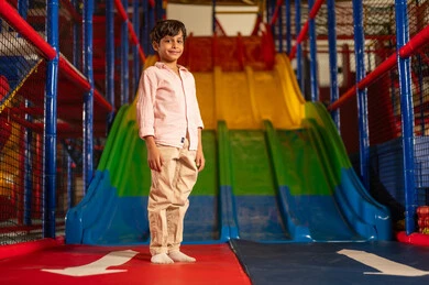 Saudi Boy Standing at Indoor Playground Slide