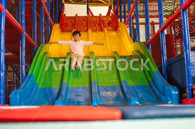 Arab Boy Sliding in Indoor Playground