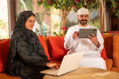 Omani Couple Using Laptop and Tablet Indoors