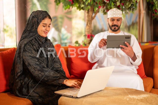 رجل وامرأة من عمان يستخدمان المحمول والجهاز اللوحي