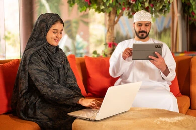 Omani Couple Using Laptop and Tablet Indoors
