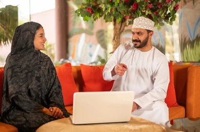 Omani Couple in Traditional Dress Using Laptop Indoors