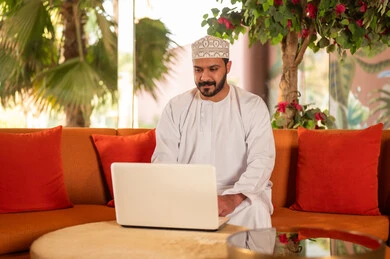 رجل عماني بالزي التقليدي يستخدم الحاسوب المحمول