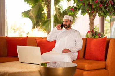 رجل عُماني بالزي التقليدي يستخدم اللابتوب والهاتف