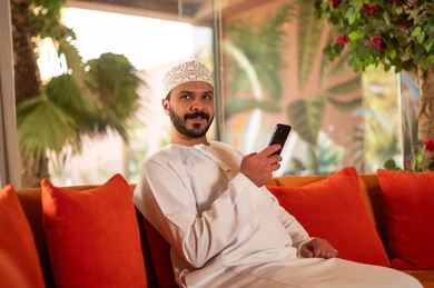 Omani Man in Traditional Dress Using Smartphone Indoors