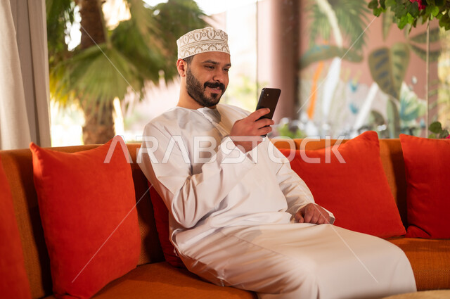 Omani Man Using Smartphone on Sofa Indoors