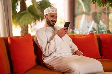 Omani Man Using Smartphone on Sofa Indoors