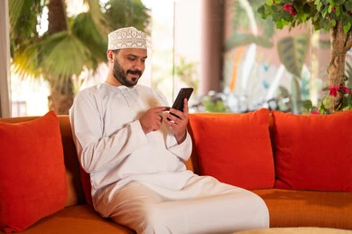 Omani Man Using Smartphone on Orange Sofa