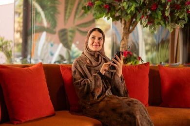 امرأة سعودية بالعباءة تستخدم الهاتف الذكي على الأريكة
