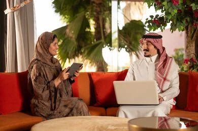 Saudi Couple Using Laptop and Tablet Indoors