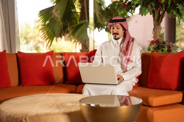 رجل سعودي يستخدم اللابتوب على أريكة برتقالية