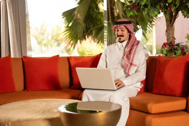 رجل سعودي بالثوب التقليدي يستخدم الكمبيوتر المحمول