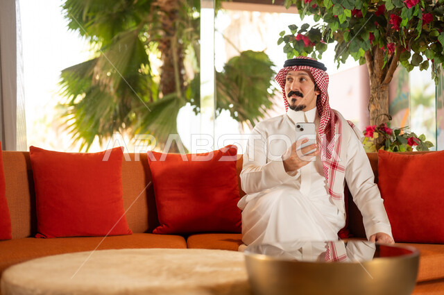 رجل سعودي بالزي التقليدي يستخدم الهاتف الذكي