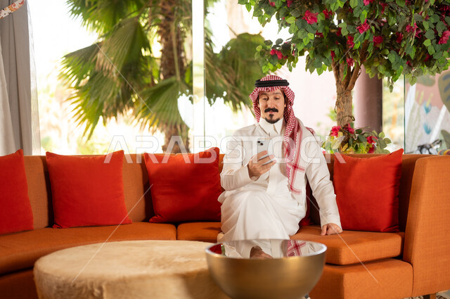 Saudi Man in Traditional Dress Using Smartphone Indoors