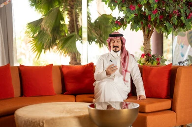 رجل سعودي بالزي التقليدي يستخدم الهاتف الذكي في الداخل