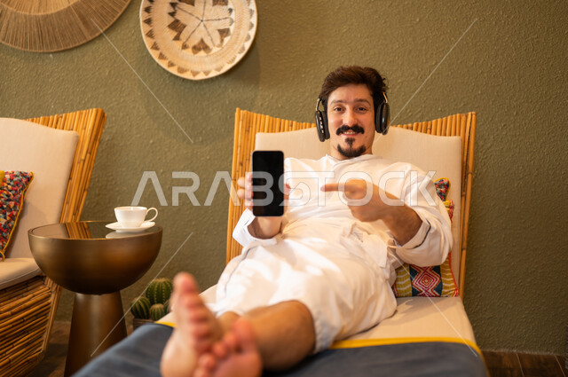Arab Man in Bathrobe Holding Smartphone with Headphones