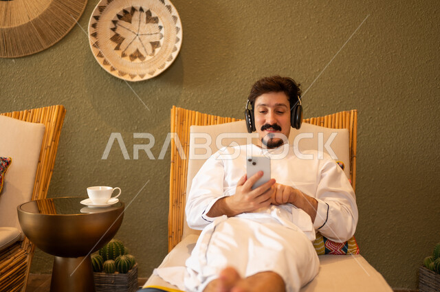 رجل سعودي بالثوب يستخدم الهاتف مع سماعات الرأس