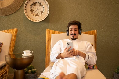 رجل سعودي بالثوب يستخدم الهاتف مع سماعات الرأس