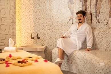 رجل عربي يرتدي رداء حمام يستجم في غرفة بخار