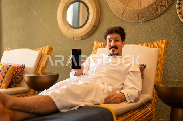 Arab Man in White Bathrobe Holding Smartphone in Spa