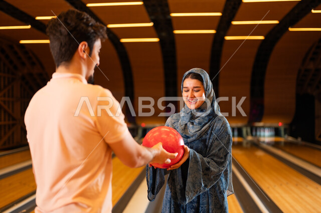 Arab Couple Holding Red Bowling Ball in Indoor Alley