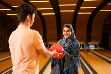Arab Couple Holding Red Bowling Ball in Indoor Alley