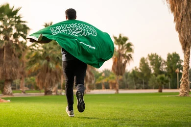 شاب سعودي يركض بالعلم في الحديقة وقت الغروب
