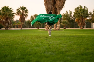 Saudi Boy Running with National Flag in Park at Sunset
