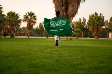 شخص سعودي يركض بالعلم في حديقة وقت الغروب