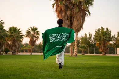 امرأة سعودية بالعلم تمشي في منتزه أخضر