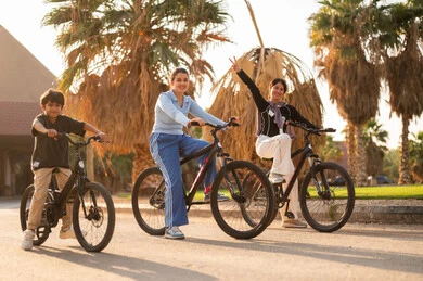 Arab Siblings Cycling Under Palm Trees at Sunset