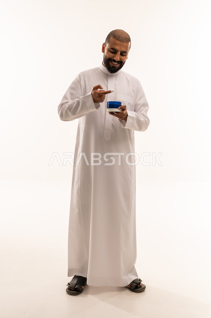 رجل عربي بالثوب الأبيض يحمل عبوة كريم العناية بالبشرة