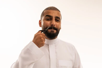 رجل سعودي يقلم شاربه بالمقص على خلفية بيضاء